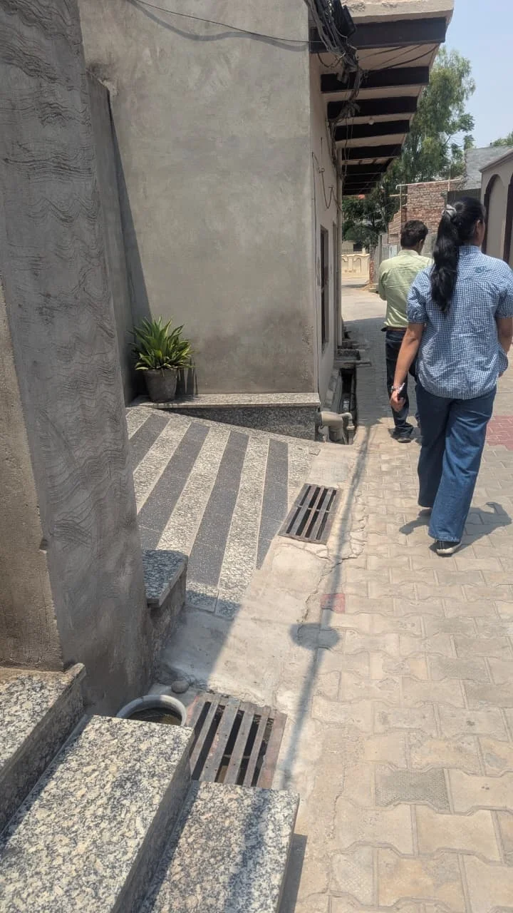 Two team members walking through a narrow village lane in Rurka Kalan